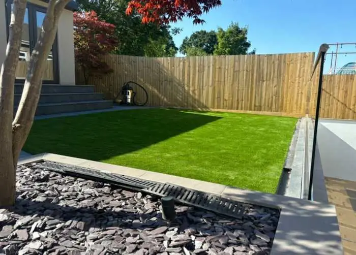 Modern back garden with new artificial lawn, slate borders and timber fencing
